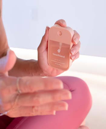 Person holding a Touchland hand sanitizer, preparing to apply it