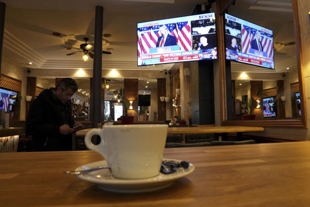 A man checks his smartphone in a cafe as a television screen shows Donald Trump,Wednesday, Nov. 6, 2024 in Paris. (AP Photo/Aurelien Morissard)