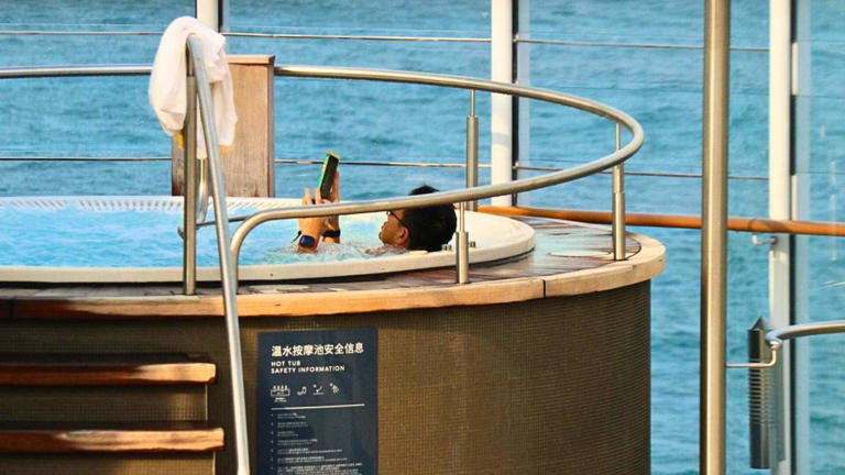A man looks through his phone while sitting in a hot tub on a cruise ship.Image source: Shutterstock