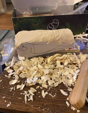 Wood carving in progress with shavings and a carved block featuring an outline of a bird, on a table