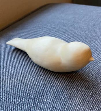 A small, smooth bird sculpture sitting on a textured surface