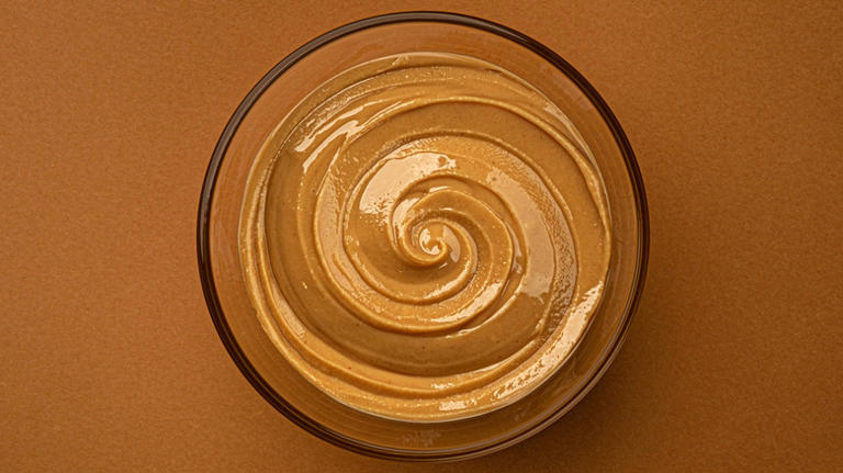 Swirl of peanut butter in glass bowl on brown table