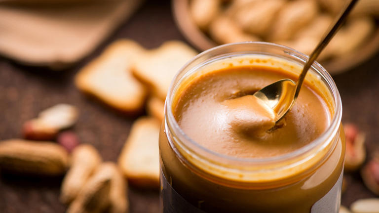 Open jar of peanut butter with spoon inside