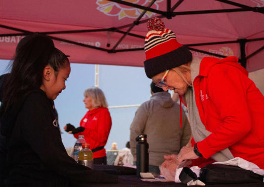 A Fiesta Bowl volunteer assists a young participant with registration and hands out camp t-shirts at the SRPMIC Baseball Fields on November 6, 2024, in Scottsdale, Ariz. (Photo by Ethan Desjardine/Cronkite News)