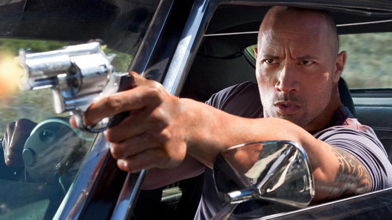 Dwayne Johnson as Jimmy Cullen firing a gun while driving in Faster