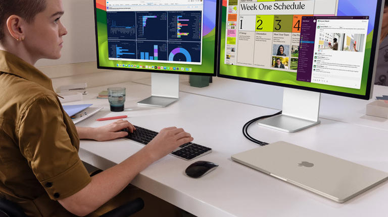 Person using a closed MacBook connected to two external monitors