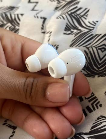 Hand holding wireless earbuds, showcasing sleek and modern design. Patterns on the fabric in the background. Featured in a shopping article