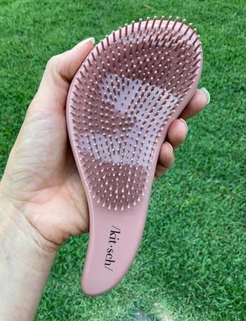 Hand holding a pink hairbrush with flexible bristles, labeled