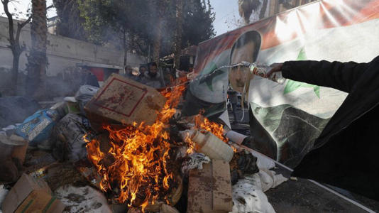 Una pancarta del derrocado Bashar al-Assad es colocada en una hoguera mientras fuerzas rebeldes destruyen drogas y alcohol, encontrados en un edificio complejo, en Damasco, Siria, miércoles 25 de diciembre de 2024.