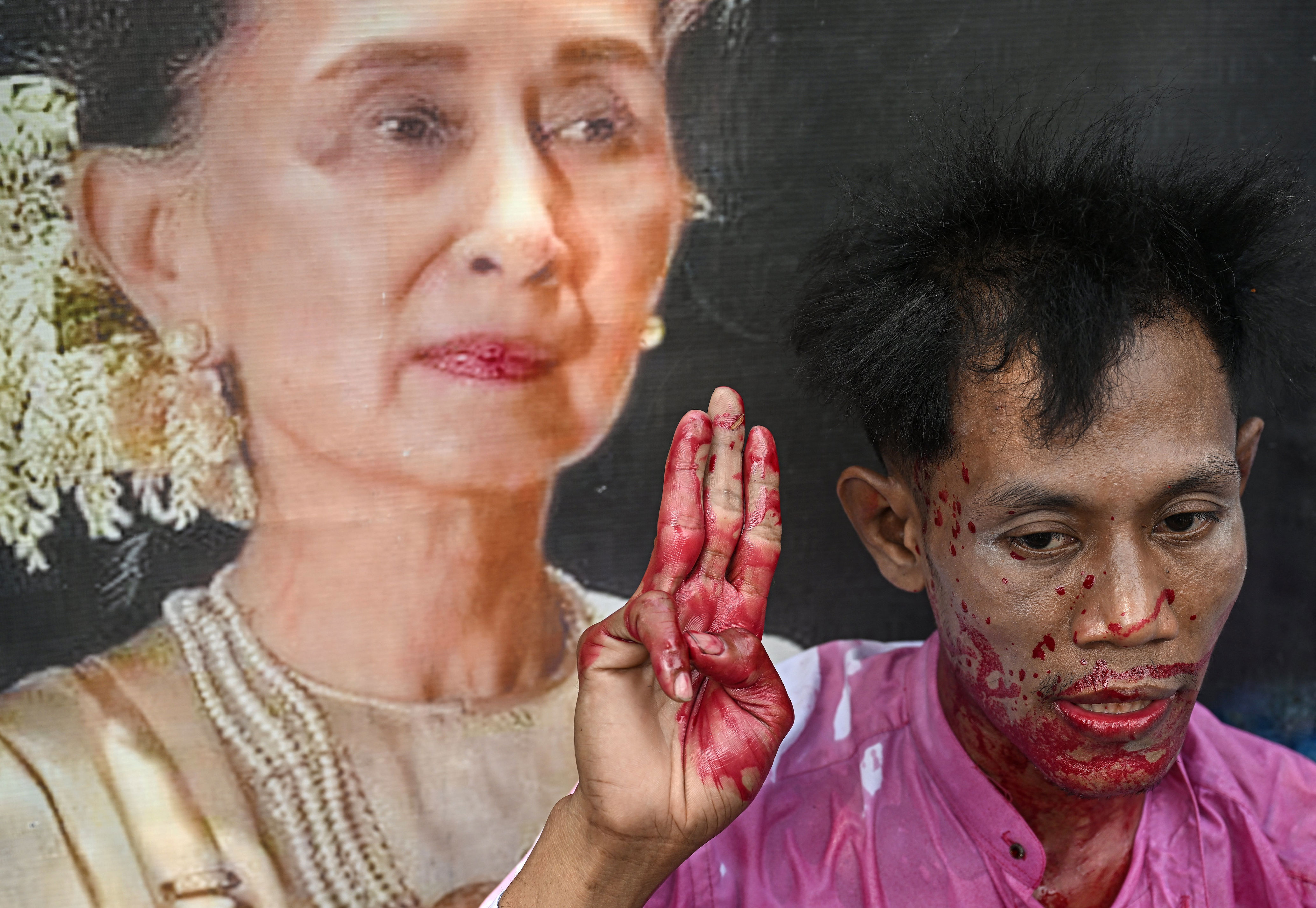 A protester covered in fake blood next to an image of detained leader Aung San Suu Kyi during a demonstration outside the UN office in Bangkok (AFP via Getty)