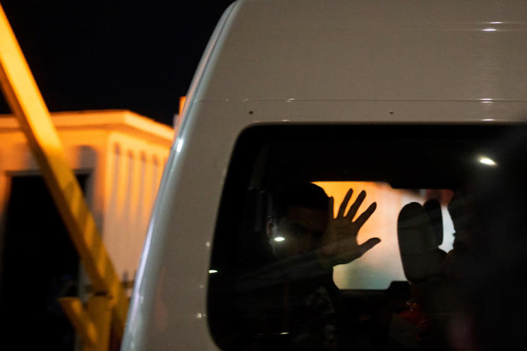 Migrants who were deported from the US to Mexico wave as they are transported to a shelter, as they cross El Chaparral pedestrian border bridge in Tijuana, Mexico, late Tuesday, Jan. 21, 2025.