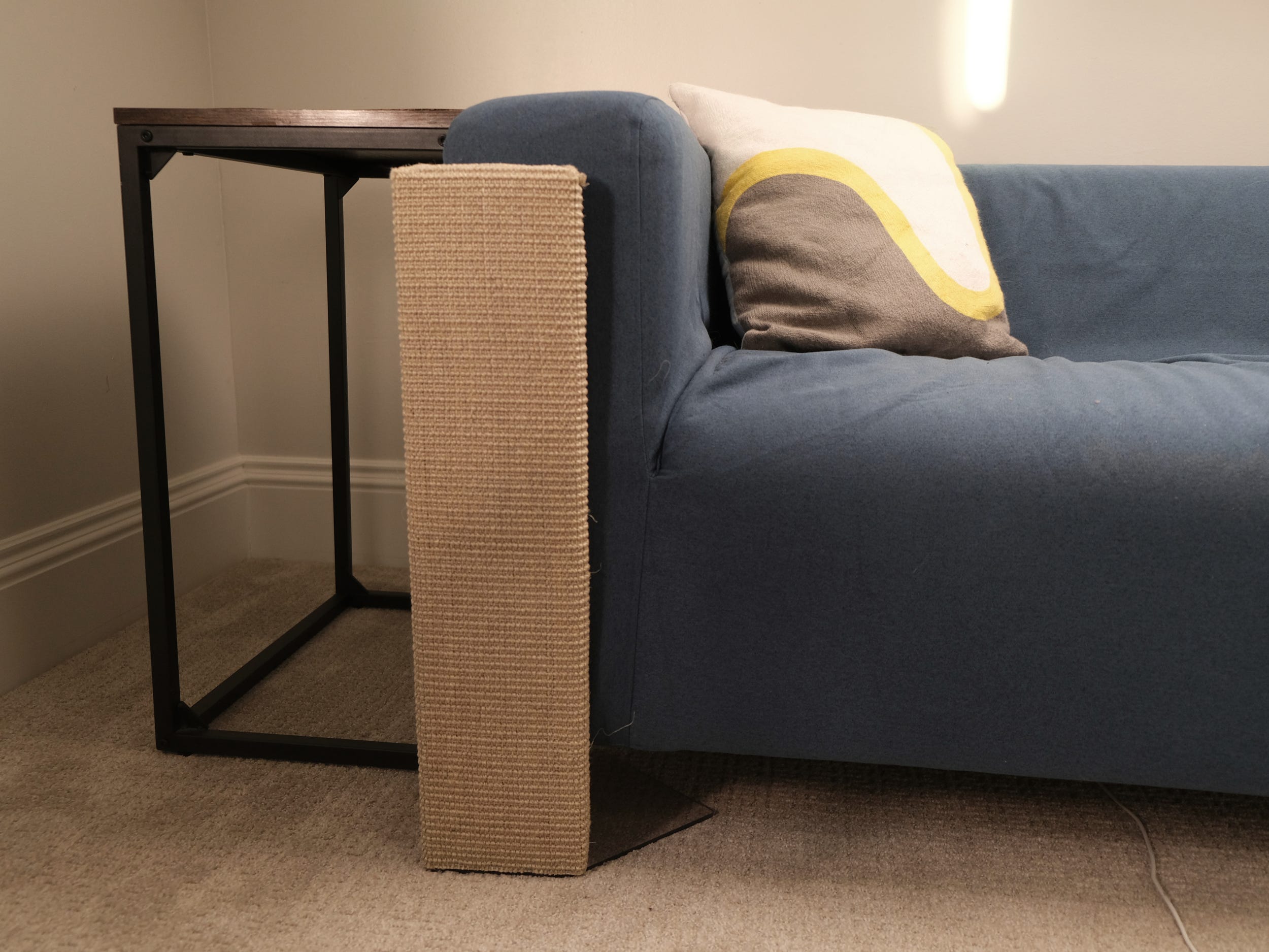 A beige sofa scratcher squared sisal furniture protector is flush against the arm of a sofa.