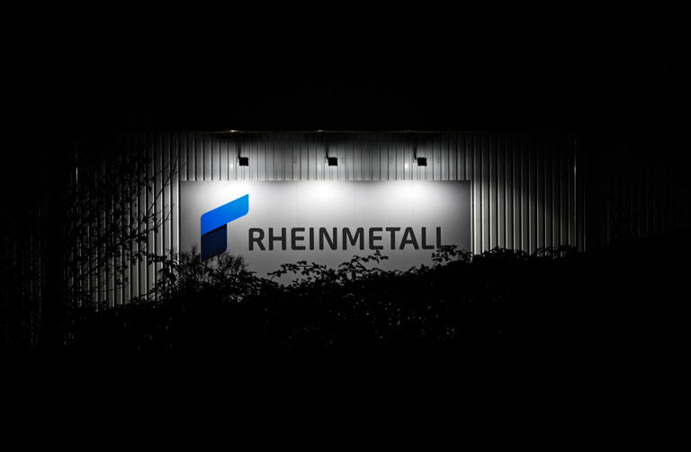 Das beleuchtete Logo und der Schriftzug der Rüstungsfirma Rheinmetall hängt an einer Produktionshalle.