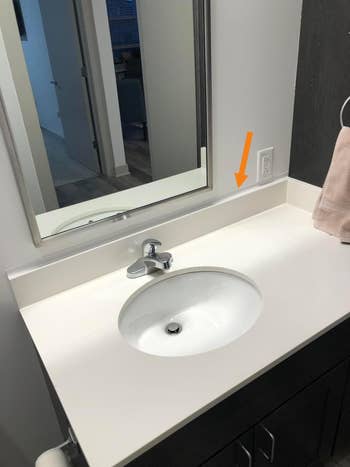 Modern bathroom vanity with a white countertop, oval sink, and mirror; a beige towel hangs nearby