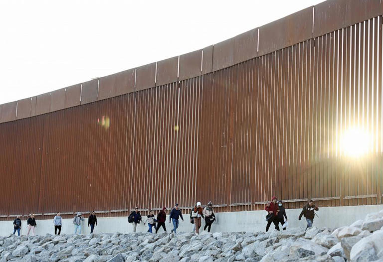 Immigrants seeking asylum in the United States walk along the border fence as the sun rises on their way to be processed by U.S. Border Patrol agents after crossing into Arizona from Mexico on May 11, 2023 in Yuma, Arizona.