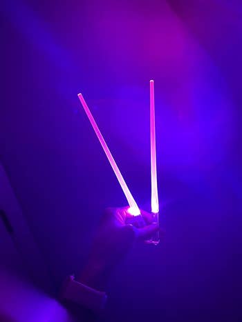 Hand holding two glowing light sticks in a dark setting, suitable for concerts or parties