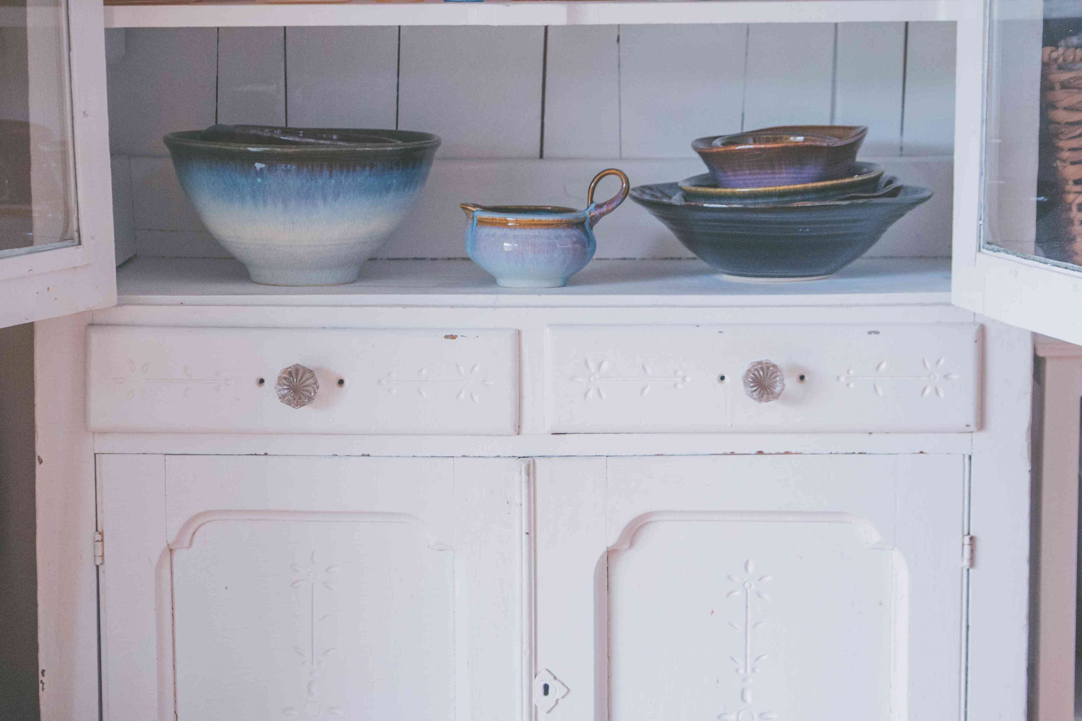 A closeup shot of ceramic kitchen pots and plates on shelves and drawers