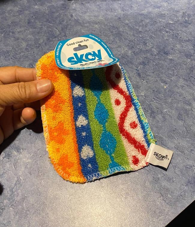 Person holding a colorful Skoy cleaning cloth with a textured surface, suitable for purchasing consideration in a shopping context