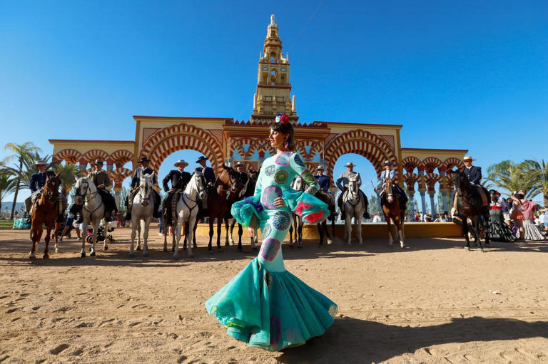 Una mujer frente a un grupo de caballos y la portada de la Feria de Córdoba. / MANUEL MURILLO