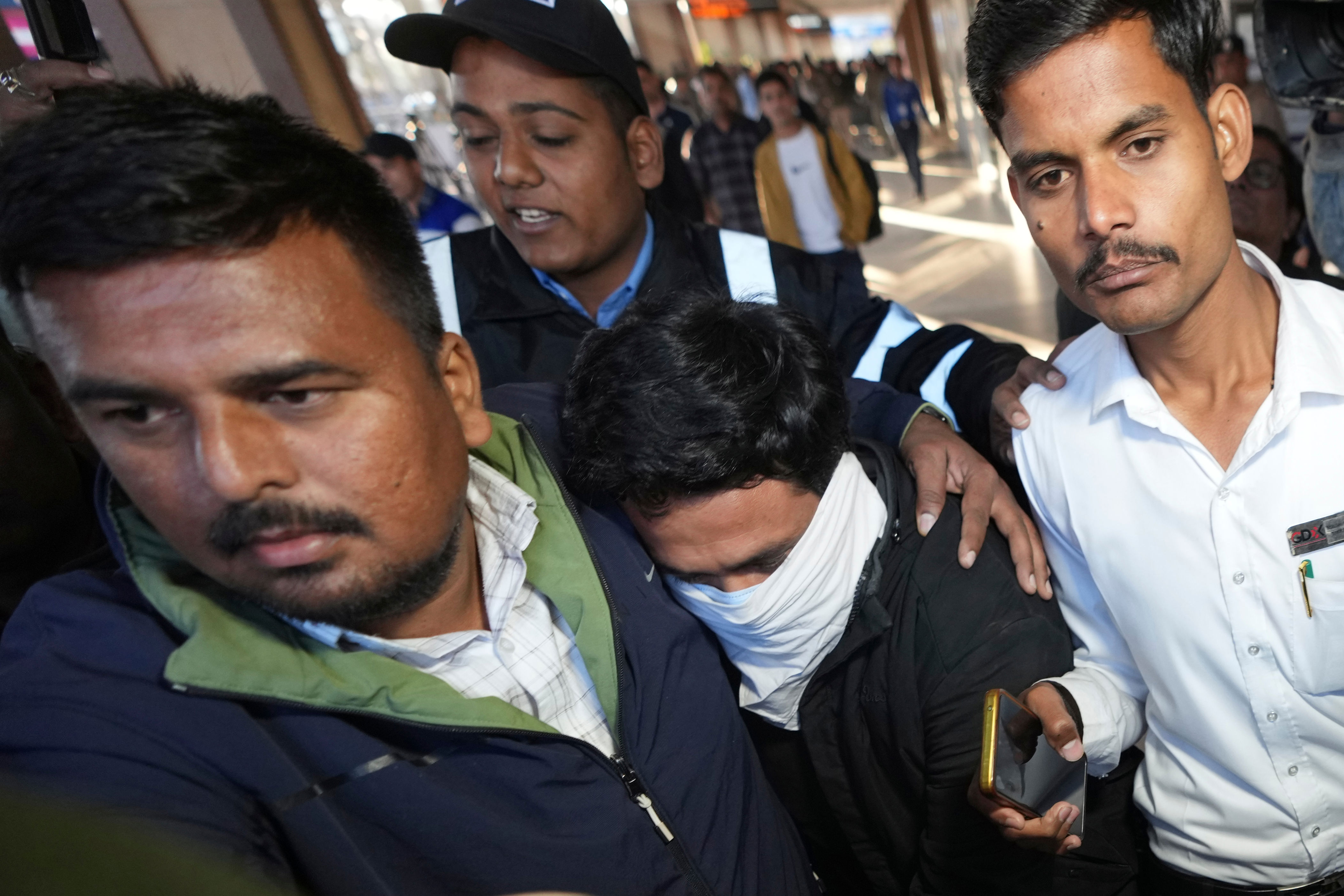 Indian police officials escort an immigrant man, center, wearing mask, deported from the United States, right, who was among those who arrived in a U.S. military plane Wednesday in Amritsar, upon his arrival at the Ahmedabad airport in India, Thursday, Feb. 6, 2025. (AP Photo/Ajit Solanki)