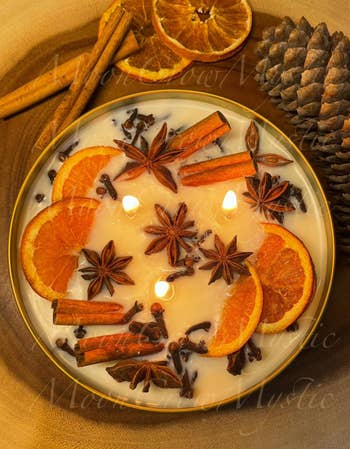 Decorative candle with dried orange slices, star anise, and cinnamon sticks, evoking a warm, cozy ambiance ideal for home decor or gifting