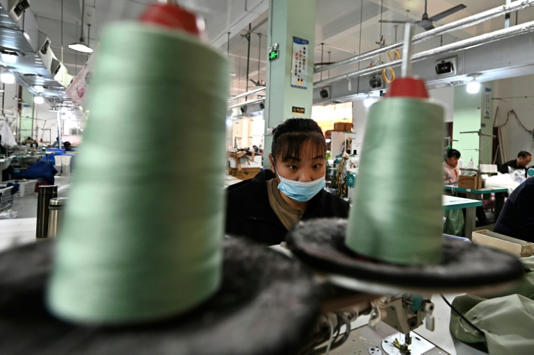 Foto tirada em 20 de fevereiro de 2025 mostra funcionária trabalhando em uma oficina de costura de roupas em Guangzhou, no sul da China