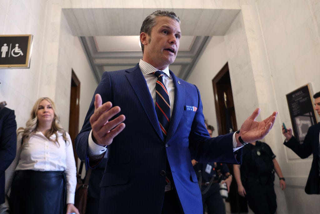 Pete Hegseth standing in a hallway surrounded by reporters.