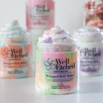 Jars of Well Etched whipped body butter, featuring colorful swirls, with product details labeled on the containers. Ideal for skincare shopping