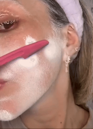 model using a pink facial razor to shave cheek
