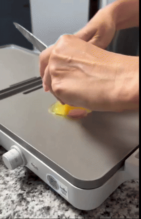 Person cracking egg on a griddle, demonstrating cooking technique