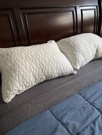 Two quilted pillows on a neatly made bed with a dark headboard and blue bedsheet