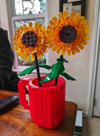 Lego sunflowers in a red brick-style mug on a wooden table indoors
