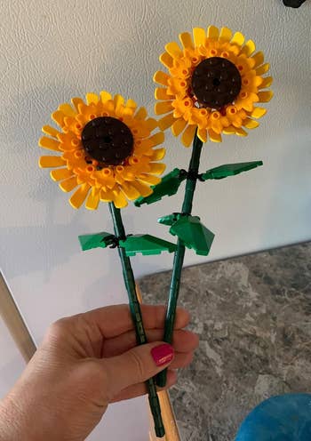 Two LEGO sunflowers with green stems and leaves held in a hand
