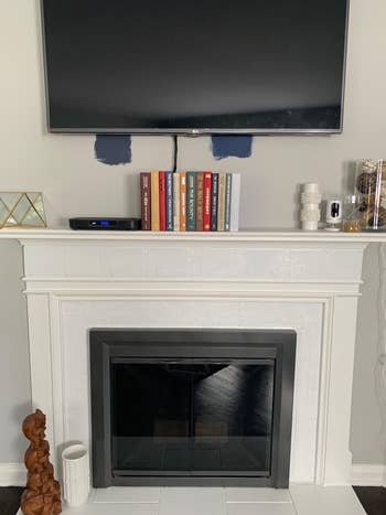 A wall-mounted TV above a fireplace with a mantel displaying books, decorative items, and candles