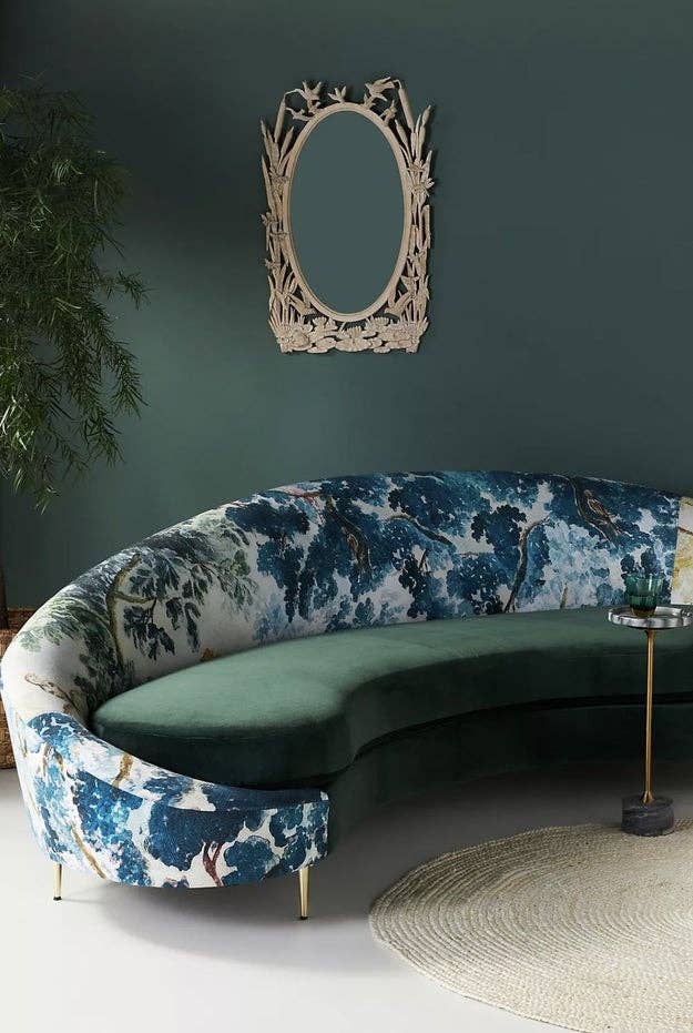 Curved velvet sofa with a nature-themed pattern in a stylish living room with a round mirror and indoor plant