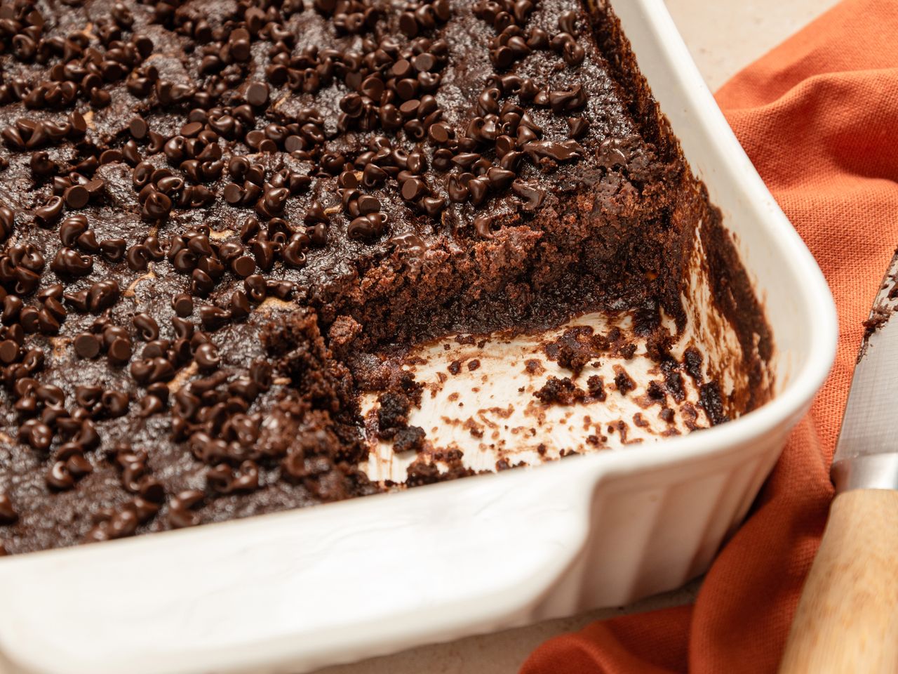A tray of chocolate dump cake with a portion removed showing its baked texture and chocolate chip topping