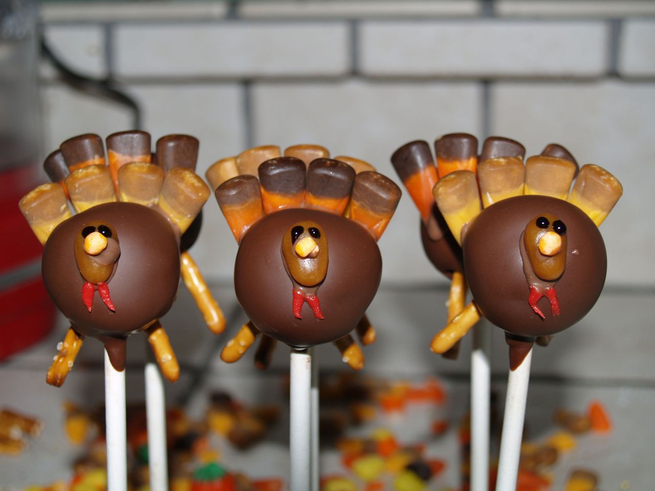 cake pops decorated to look like turkeys for Thanksgiving, with pretzel legs and candy corn tail feathers