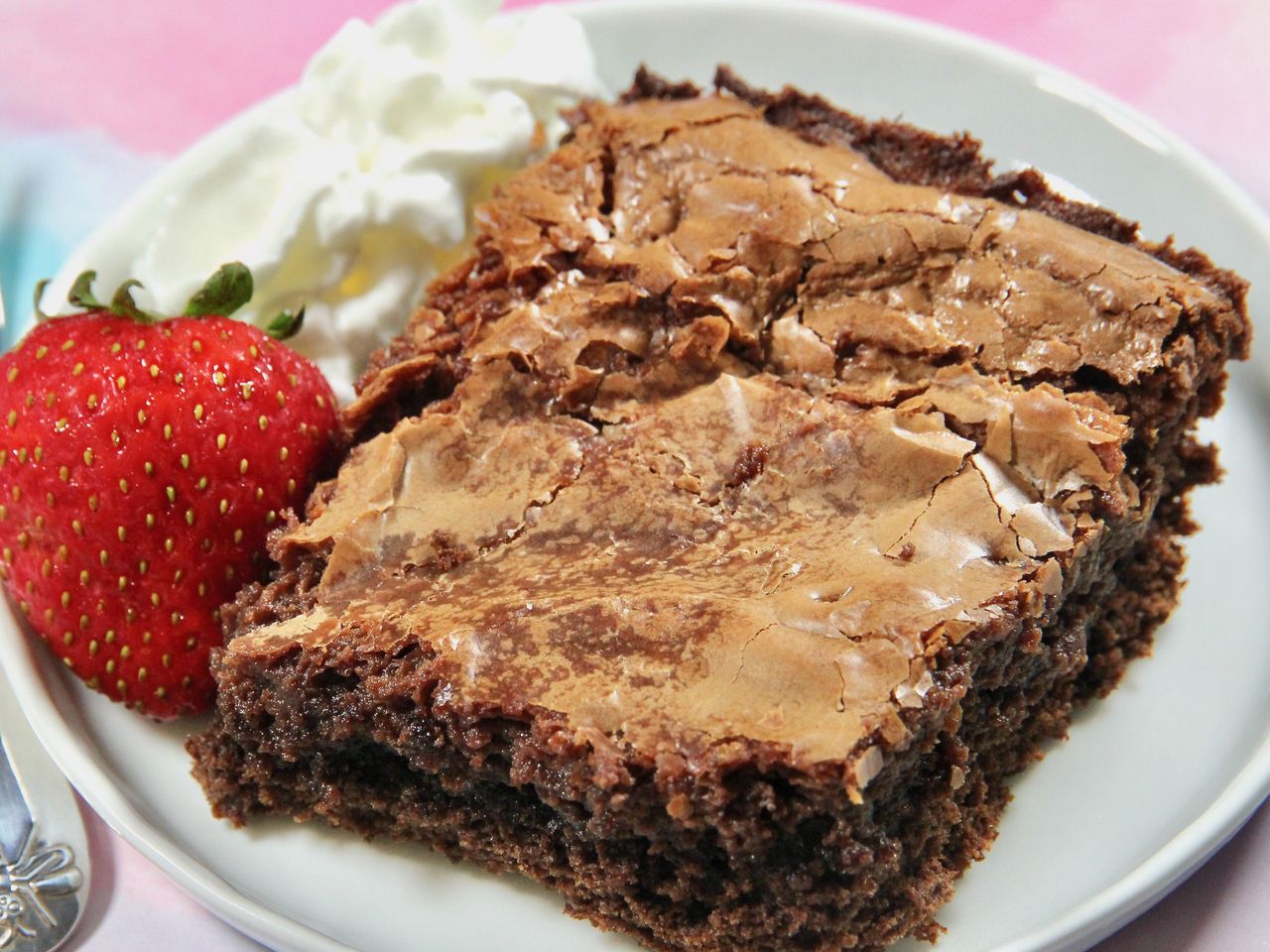 chocolate gooey butter cake on a plate with a strawberry and whipped cream