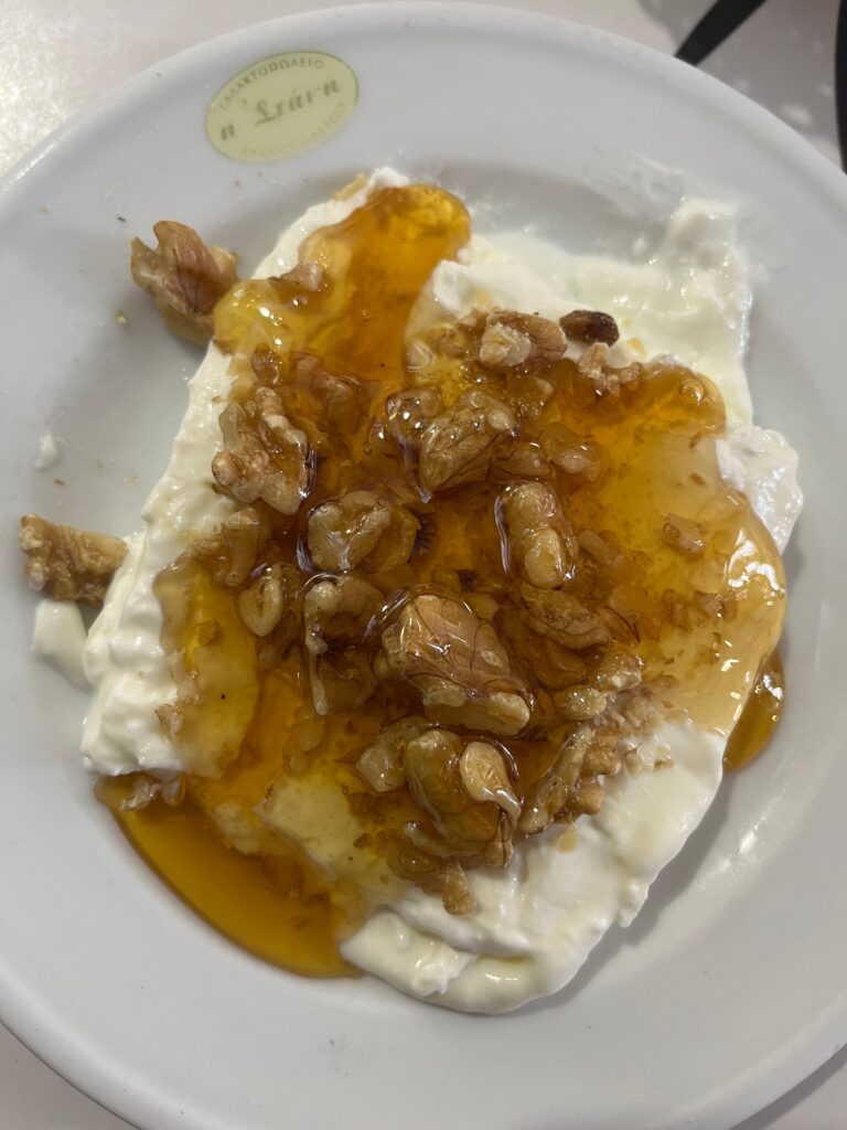 Greek yogurt topped with honey and walnuts served in a white bowl with a small label reading