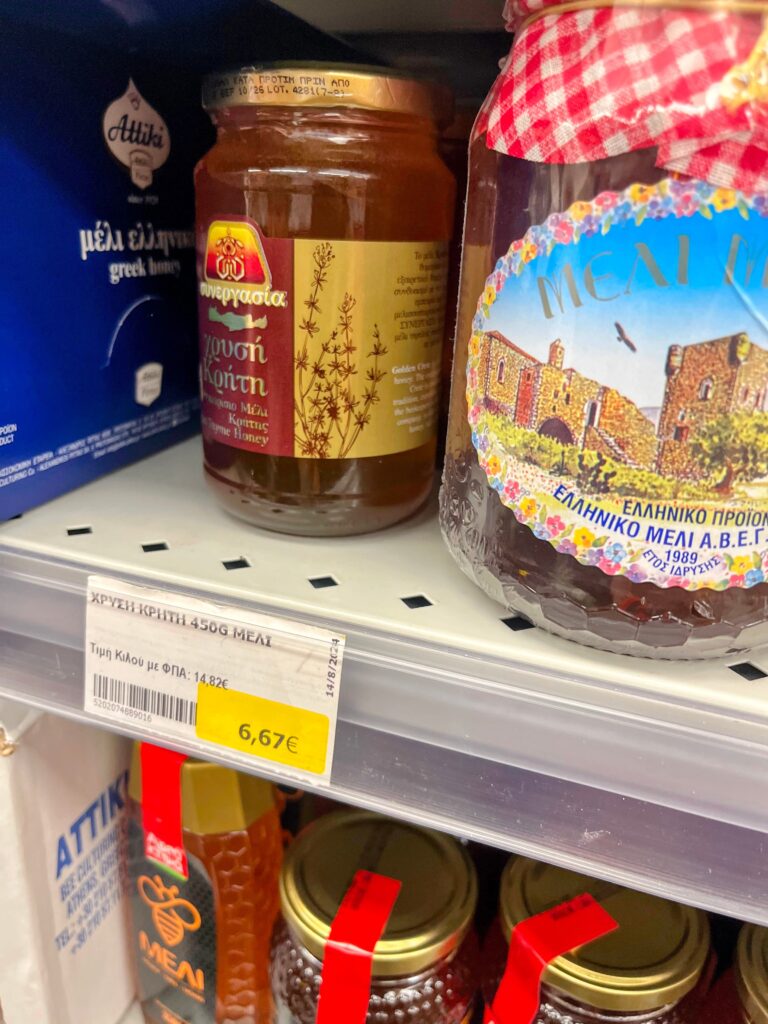 Shelves of Greek honey jars in a store with visible labels and a price tag reading