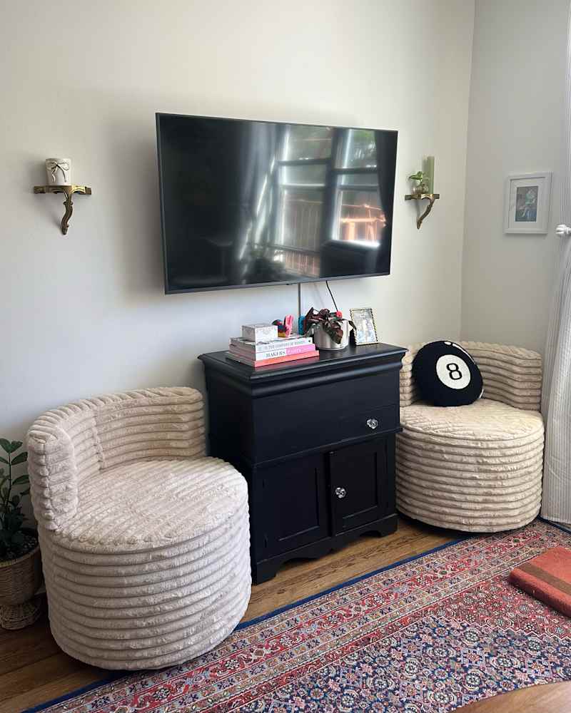Cozy living area featuring two round beige chairs, a black cabinet, a TV, and a colorful patterned rug.
