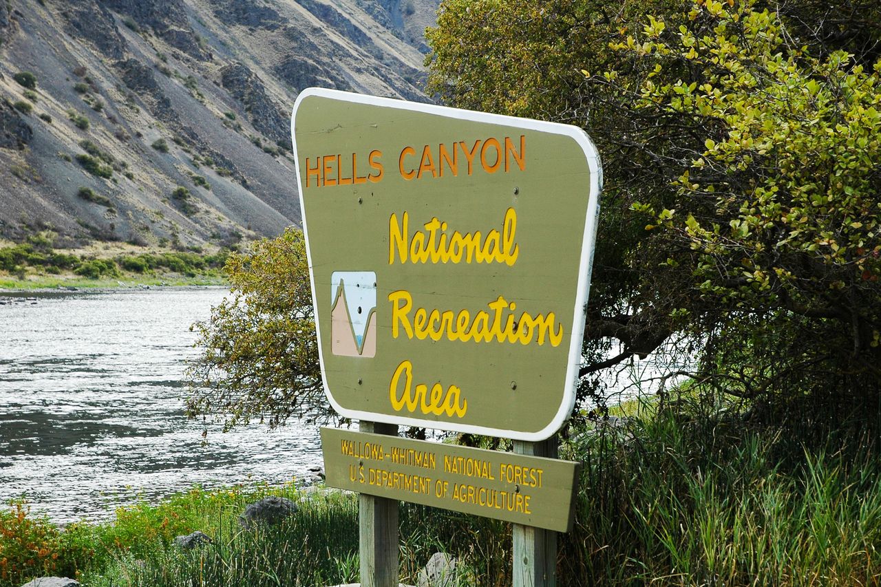 Sign reading Hells Canyon National Recreation Area with a waterway and vegetation in the background