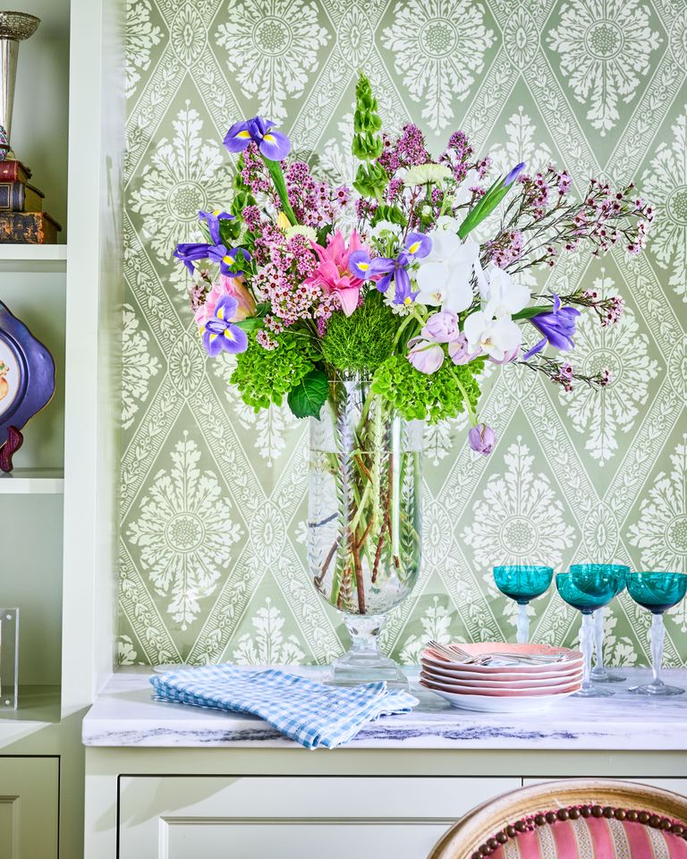 A vase with a floral arrangement placed on a countertop in a room with decorative wallpaper