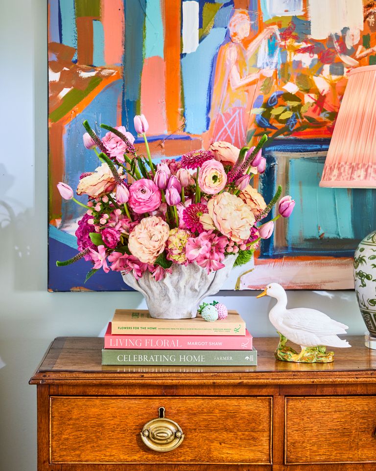 A floral arrangement on a wooden table accompanied by a decorative figurine and books with colorful artwork in the background