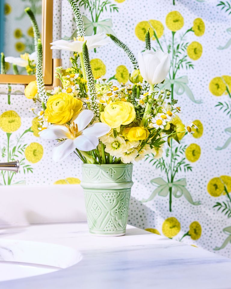 Floral arrangement in a decorated green vase placed on a counter against a patterned wallpaper background