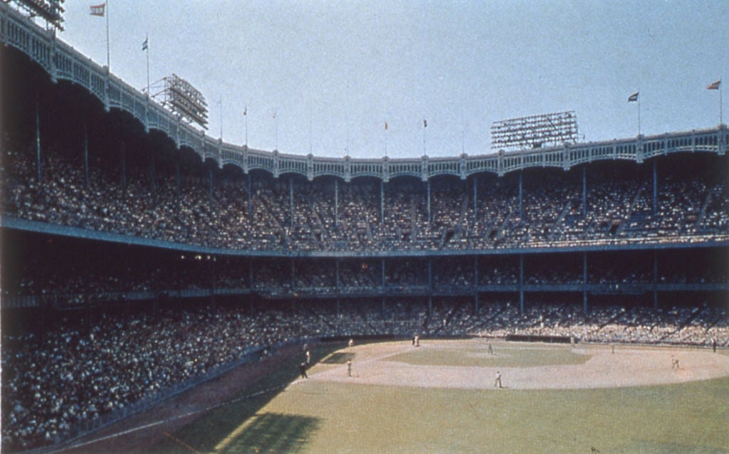 A historic baseball game is underway in a packed, classic stadium with arched details and tall lighting fixtures