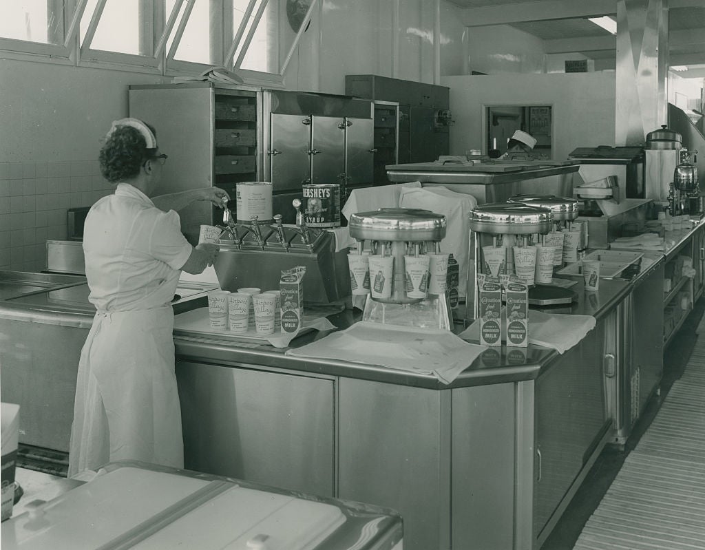 A retro ice cream shop with a server preparing orders, featuring vintage equipment and containers