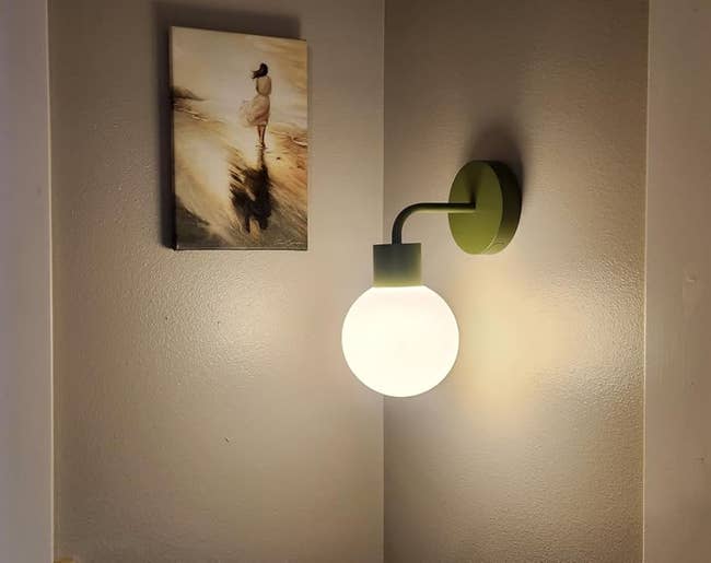 Wall sconce lit beside a small framed beach artwork, between two windows with closed blinds, creating a cozy atmosphere