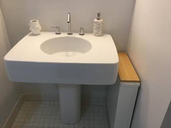 Modern bathroom sink with sleek faucet, marble soap dispenser, small decorative vase, and wooden shelf