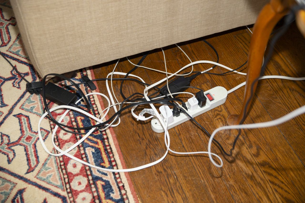 Messy electrical cords and phone charger cables on floor with surge protector power strip plugged into electrical outlet